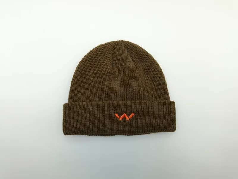 Olivgrüne Strickmütze mit Umschlagbündchen und kleinem orangenem Stickerei-Emblem, flach auf weißem Hintergrund fotografiert