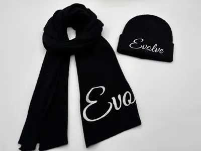 Schwarzes Rippenstrick-Winterset aus Schal und Beanie-Mütze mit weißem bestickten Kursivschrift-Aufdruck auf weißem Hintergrund