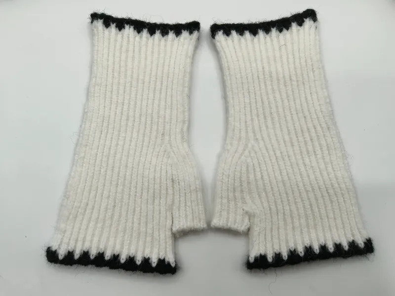 Paar weiße Rippenstrick-Fingerhandschuhe mit schwarz-weißem Zickzack-Abschlussband oben und unten, flach auf weißem Hintergrund
