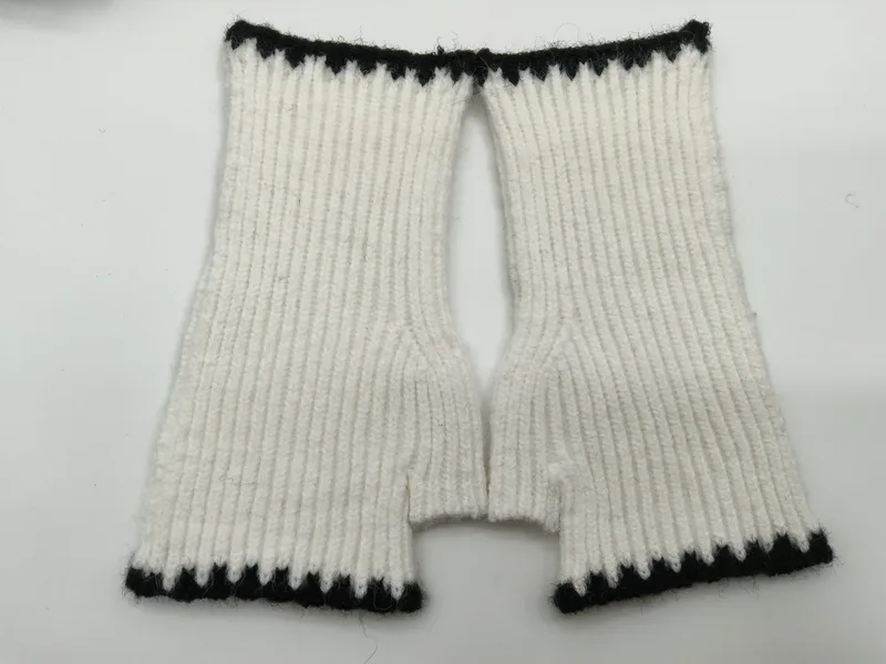 Draufsicht auf handgestrickte weiße Rippenstrick-Fingerhandschuhe mit schwarzen Kontrastbündchen an Handgelenk und Fingeröffnungen