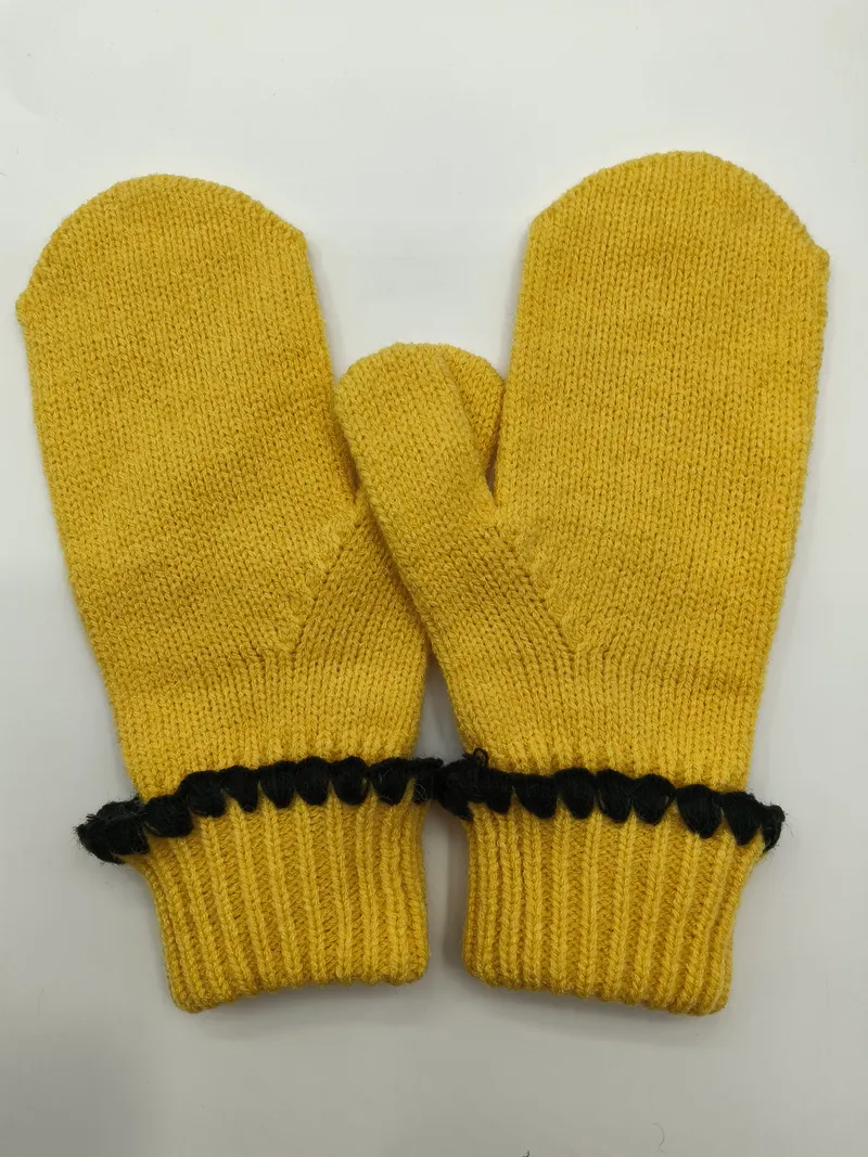 Paar senfgelbe Strickfäustlinge mit Rippenbündchen und schwarzen dekorativen Bommel-Details an den Manschetten