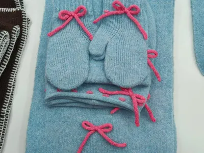 Hellblaues gestricktes Babywinter-Geschenkset mit Schal, Mütze und Fäustlingen mit rosafarbenen Schleifen-Applikationen, flach drapiert