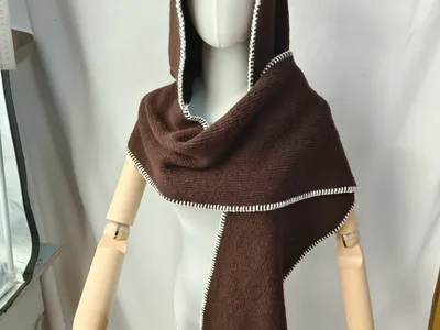 Dunkelbrauner gestrickter Kapuzenscarf-Umhang mit weißer Blanket-Stitch-Bordüre auf Schneiderpuppe mit Holzarmen