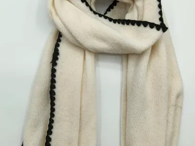 Elfenbeinfarbener gestrickter Winterschal mit dekorativer schwarzer Bogenkante, flach auf hellem Untergrund drapiert