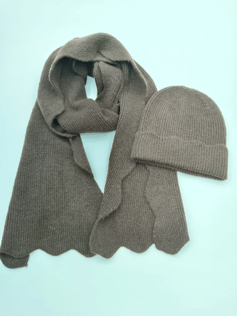 Taupefarbenes Rippenstrick-Set mit langem Schal mit Wellensaum und passender Umschlag-Beanie auf hellem Untergrund