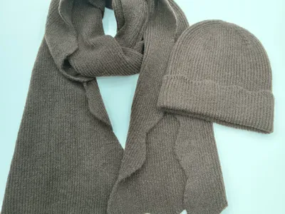 Taupefarbenes Rippenstrick-Set mit langem Schal mit Wellensaum und passender Umschlag-Beanie auf hellem Untergrund