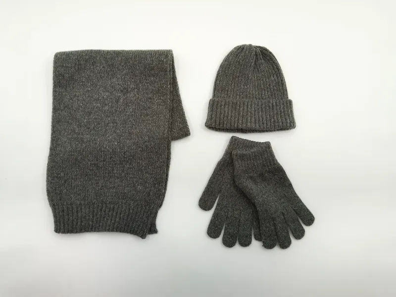 Flach drapiertes graues Strick-Accessoire-Set mit Schal, Beanie-Mütze und Handschuhen auf weißem Untergrund