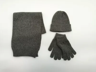Flach drapiertes graues Strick-Accessoire-Set mit Schal, Beanie-Mütze und Handschuhen auf weißem Untergrund