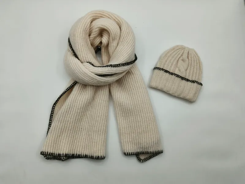 Creme-weißes Strick-Set aus gerolltem Schal und Beanie mit auffälliger schwarzer Festonstich-Borte auf weißem Untergrund