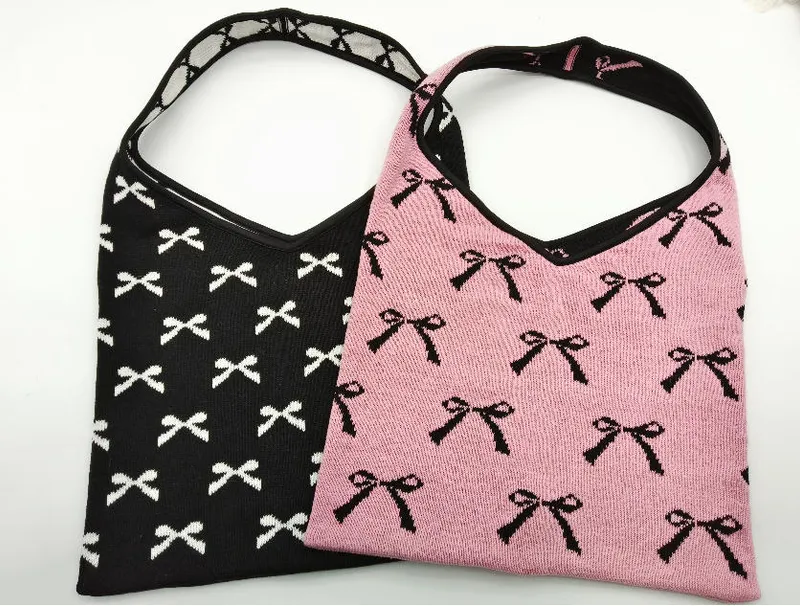Zwei gestrickte Hobo-Bags mit Allover-Schleifenmuster: eine schwarz mit weißen Schleifen, eine pink mit schwarzen Schleifen, mit Schulterriemen