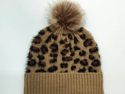 Kamelbraune gestrickte Beanie im Leopardenprint mit fluffigem Kunstpelz-Bommel auf der Spitze – Draufsicht auf weißem Hintergrund