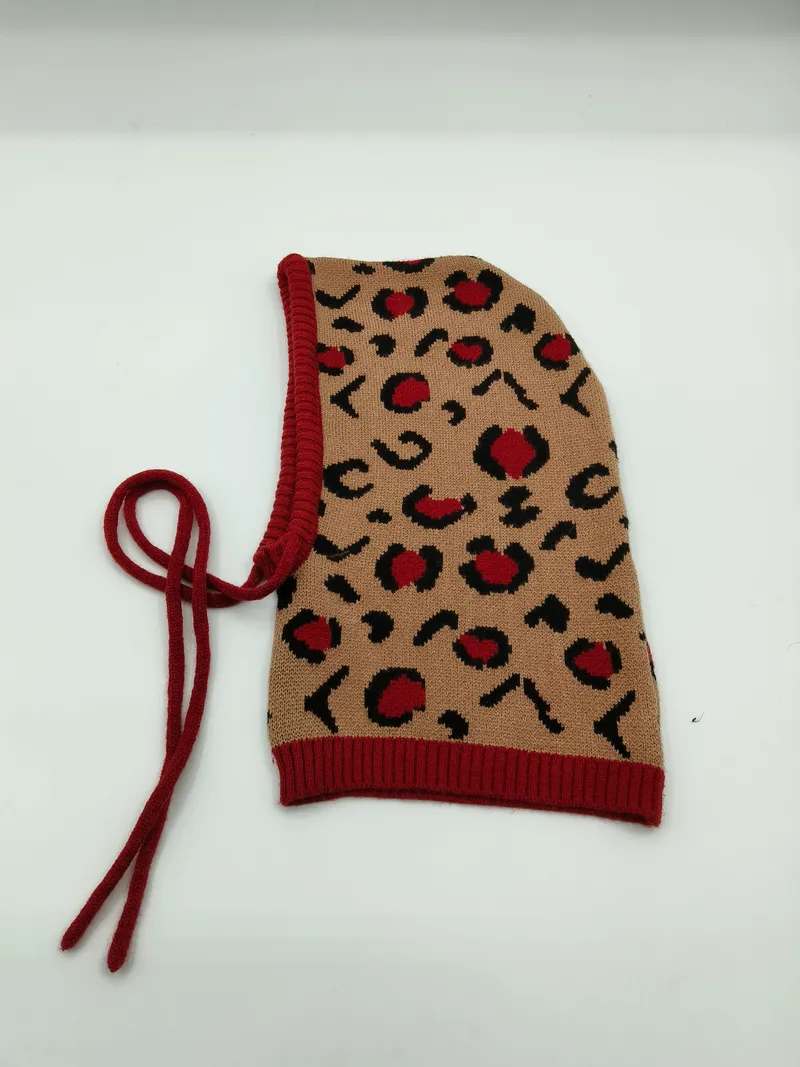 Beige-rote gestrickte Sturmhaube mit Leopardenmuster, rotem Rippensaum und Schnürbändern zum Binden – Flachansicht auf weißem Hintergrund