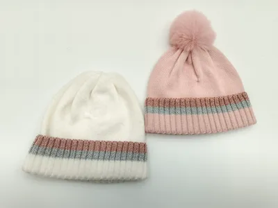 Zwei Rippenstrick-Beanies in Weiß und Rosa mit schimmernden Metallic-Streifen am Umschlag – pinke Mütze mit Kunstfell-Bommel obenauf