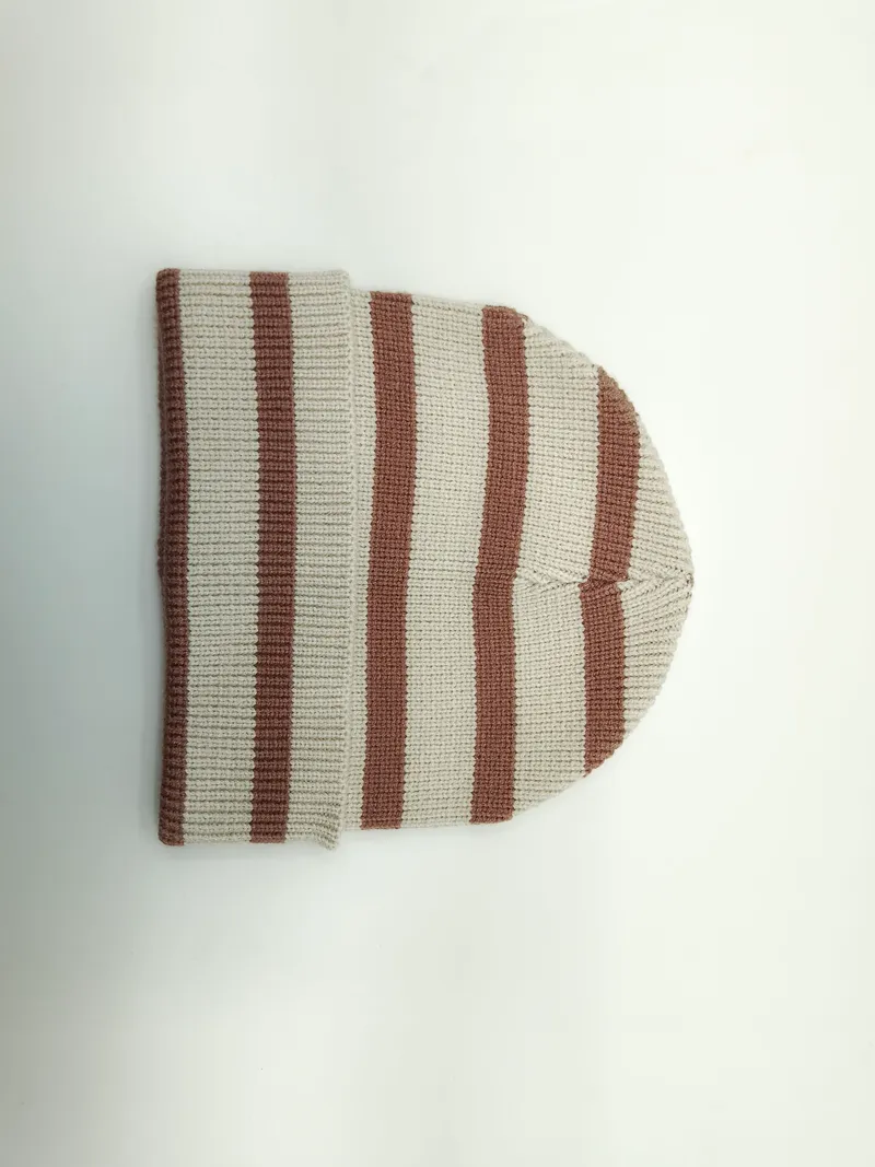 Flach aufgelegte Rippenstrickmütze mit abwechselnden Streifen in Creme und Sandbraun, umgeklapptes Bündchen auf weißem Hintergrund