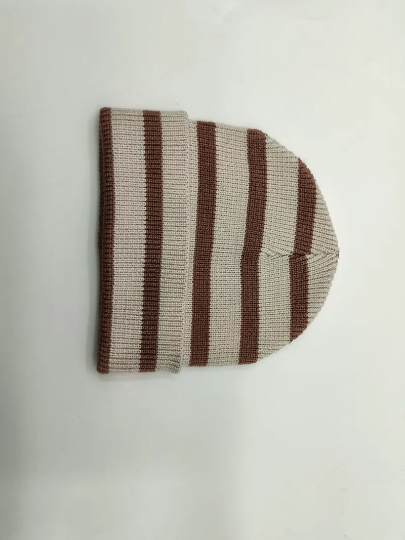 Gefaltete Rippenstrickmütze mit horizontalen Streifen in Braun und Naturweiß auf weißem Untergrund – Detailansicht der Strickstruktur