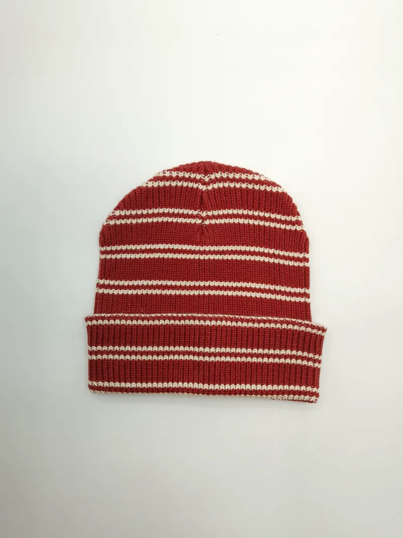 Flach gelegte Rippenstrickmütze mit horizontalen Streifen in Terrakotta-Rot und Cremeweiß sowie gefalteter Krempe auf weißem Hintergrund