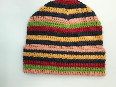 Handgefertigte Häkelmütze mit breiten Farbstreifen in Pink, Grün, Rot, Gelb und Schwarz, strukturiertes Häkelmuster auf weißem Hintergrund