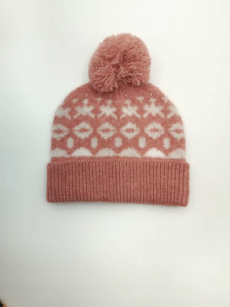 Rosafarbene Strickmütze mit weißen geometrischen Schneeflocken-Ornamenten und flauschigem Bommel, Produktfoto auf hellem Hintergrund