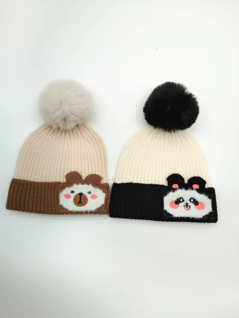 Zwei Strickmützen mit Bommeln: hellbraune Bärenmütze mit Cartoon-Bärengesicht und schwarz-cremefarbene Pandamütze mit Panda-Applikation