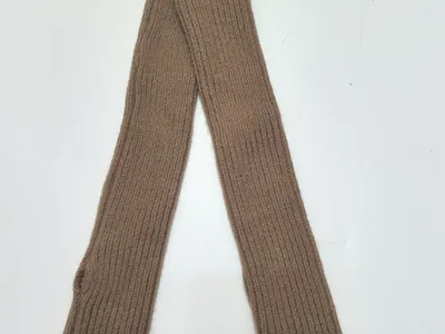 Langes Paar fingerloser Armstulpen aus weichem Rippenstrick in warmem Kamelbraun, flach auf hellem Untergrund fotografiert