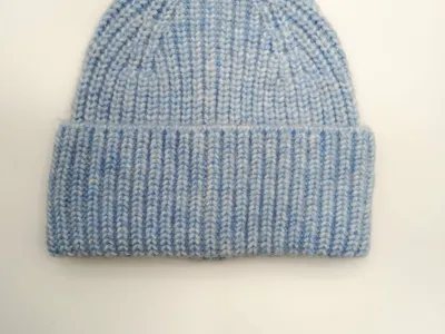 Pastellblaue Strickmütze mit strukturiertem Marl-Garn und umgeklapptem Rand, von oben fotografiert auf weißem Hintergrund