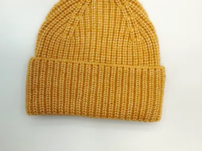 Senfgelbe Strickmütze mit breitem gefalteten Bund aus Rippenstrick, flach auf weißem Untergrund fotografiert