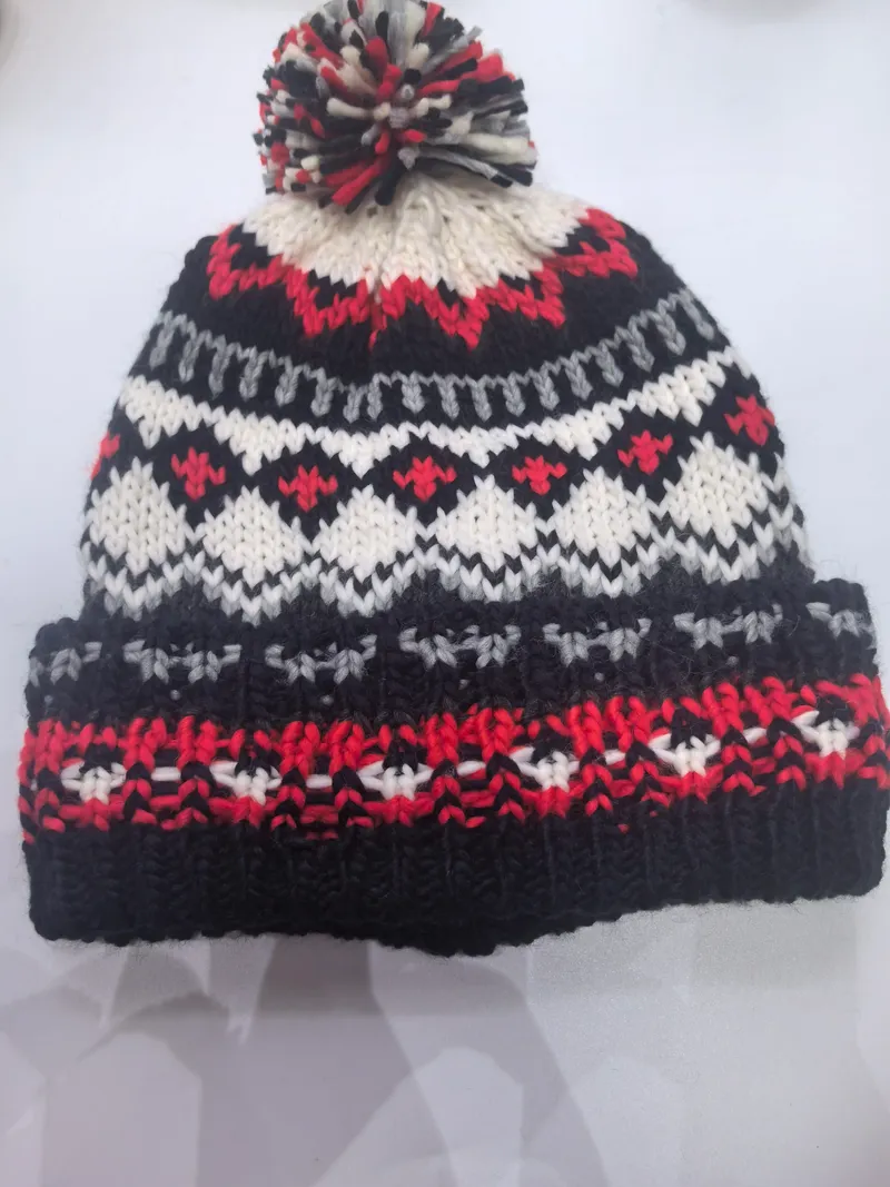 Handgestrickte Fair-Isle-Wintermütze in Schwarz, Rot, Weiß und Grau mit buntem Wollbommel auf der Spitze