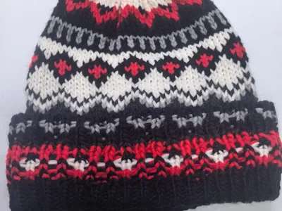 Handgestrickte Fair-Isle-Wintermütze in Schwarz, Rot, Weiß und Grau mit buntem Wollbommel auf der Spitze