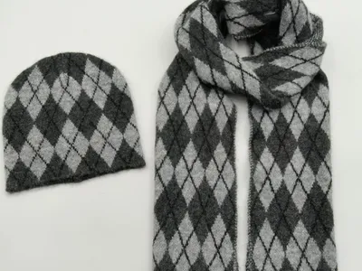 Aufeinander abgestimmtes Strickset aus Mütze und Schal mit Argyle-Rautenmuster in Anthrazit und Hellgrau, Draufsicht auf weißem Hintergrund