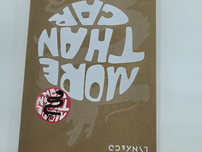 Umgekehrte braune Kraftpapier-Geschenkbox mit weißem Schriftzug 'More Than Core', Drachen-Aufkleber und Lynk & Co-Winteranzug-Branding