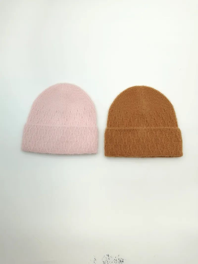 Zwei flauschige Wintermützen mit Umschlagbund nebeneinander, eine in zartem Rosa und eine in warmem Kamelbraun, Draufsicht auf weißem Untergrund
