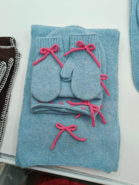 Hellblaues gestricktes Babywinter-Geschenkset mit Schal, Mütze und Fäustlingen mit rosafarbenen Schleifen-Applikationen, flach drapiert