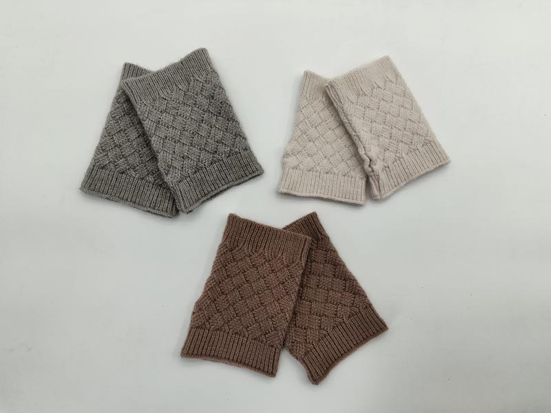 Drei Paar fingerlose Handschuhe mit Korbflechtmuster in den Farben Grau, Cremeweiß und Braun, flach auf weißem Untergrund angeordnet
