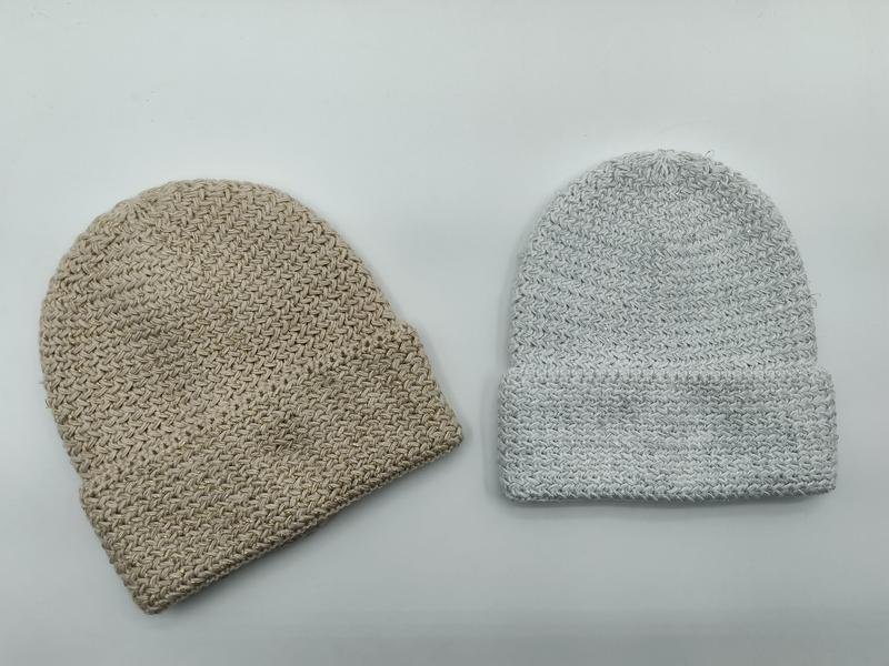 Zwei grob gestrickte Beanies nebeneinander: eine beige ohne Krempe und eine hellgraue mit umgeschlagenem Rand, auf weißem Hintergrund