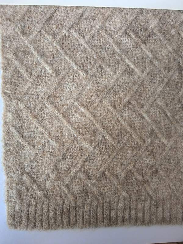 Nahaufnahme einer beigefarbenen Wollmisch-Wurfdecke mit Rautengitterstrickmuster und geripptem Rand
