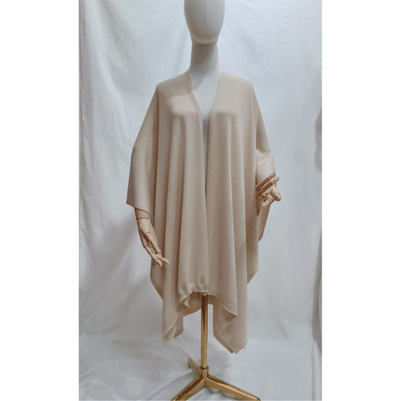 Beigefarbener, oversized Strickponcho mit offenem Vorderteil und geripptem Abschluss, drapiert auf einer Schneiderpuppe in neutralem Ton