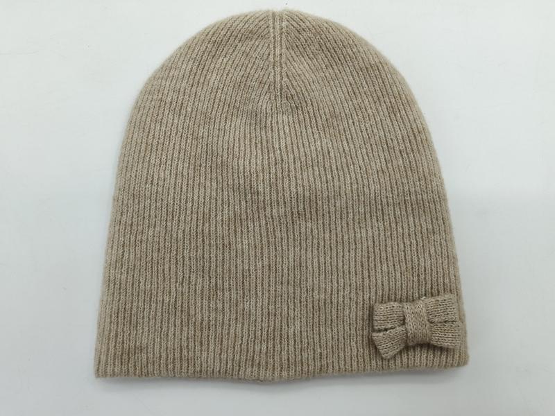 Hellbeige Strickmütze mit feiner Rippentextur und kleiner dekorativer Schleife an der Seite, Draufsicht auf weißem Untergrund
