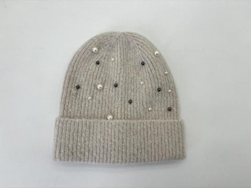 Flach liegend: Beige Rippstrickmütze mit vereinzelten weißen Perlen und dunklen Kristallnieten dekoriert, weißer Hintergrund