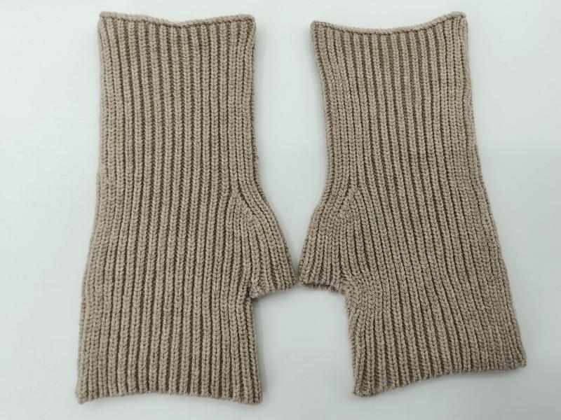 Ein Paar fingerlose Strickhandschuhe in Sandbeige mit Rippenstruktur und Daumenöffnung auf weißem Hintergrund