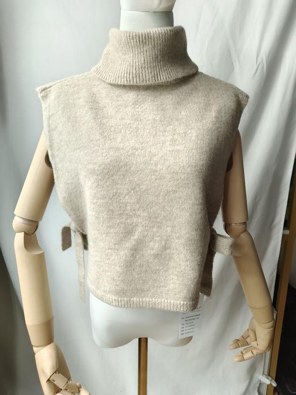 Beige ärmellose Rollkragen-Strickweste mit seitlichem Bindedetail auf einer Modelpuppe, weicher Wollmix