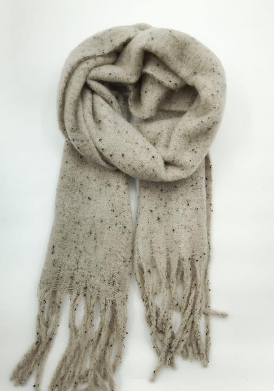 Cremefarbener Schal mit dunklen Sprenkeln aus weichem Strickgarn, locker gerollt mit Fransenzipfeln auf weißem Hintergrund
