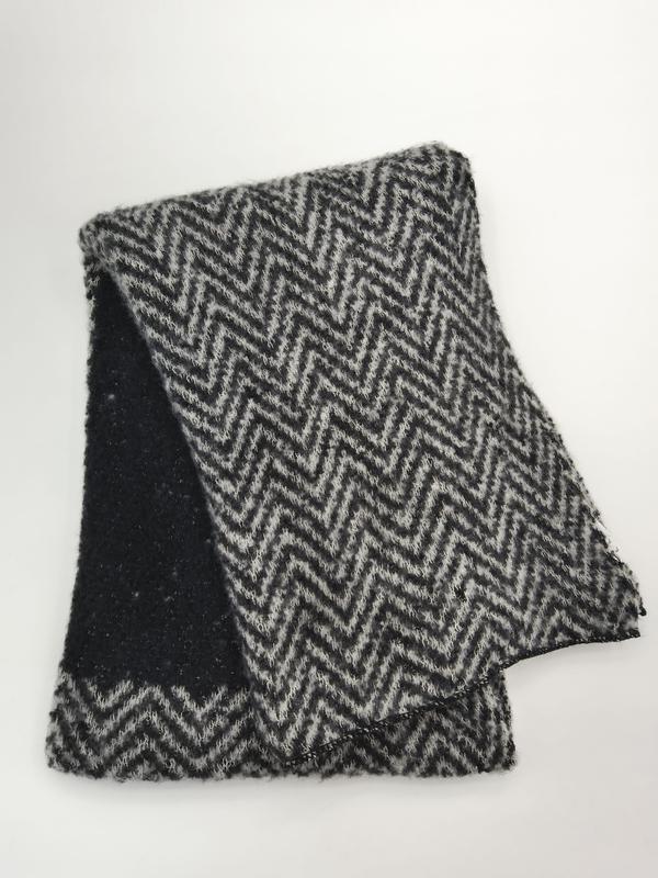 Gefalteter schwarz-grauer Strickschal mit Chevron-Zickzack-Muster und flauschiger Wollmischungs-Textur auf weißem Hintergrund