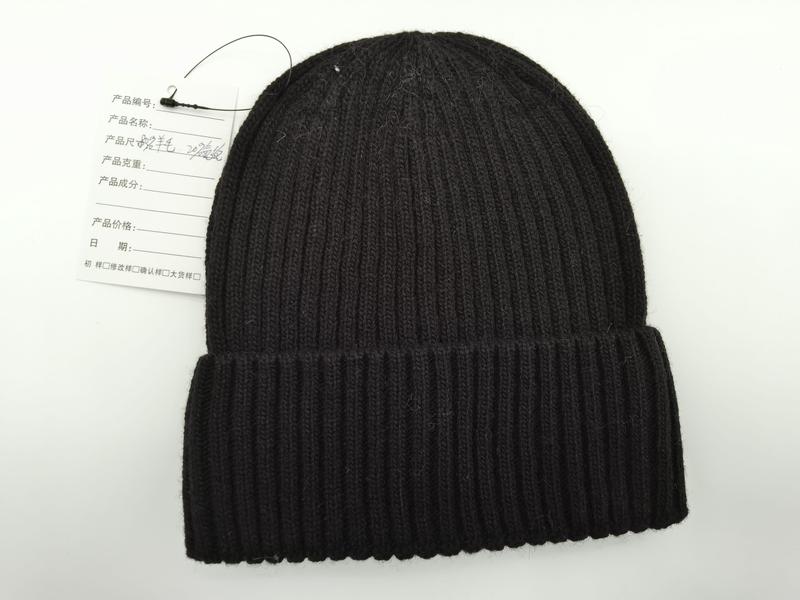 Schwarze Grobstrick-Beanie mit gefaltetem Krempenrand und angehängtem Produktetikett, Flatlay-Aufnahme auf weißem Hintergrund