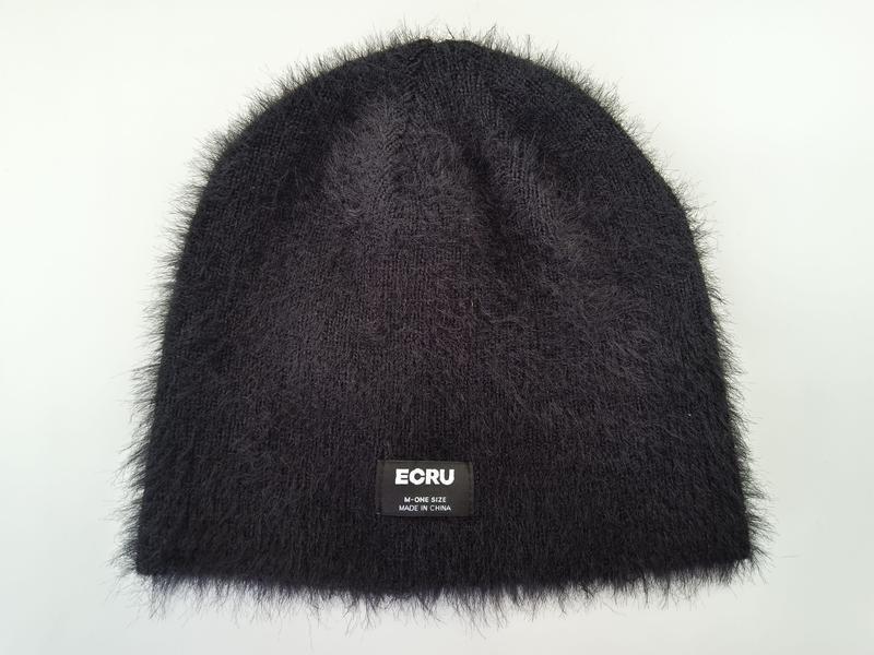 Schwarze Flauschwollmütze mit dichtem, samtartigem Strickflor und aufgenähtem Markenlabel, Draufsicht auf weißem Hintergrund
