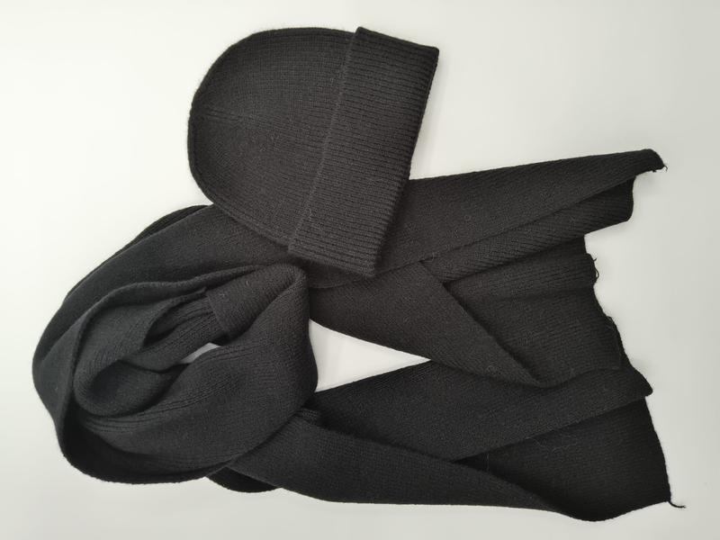 Schwarze gerippte Strickmütze mit dazu passendem langen Strickschal, flach auf weißem Hintergrund liegend, Materialstruktur sichtbar