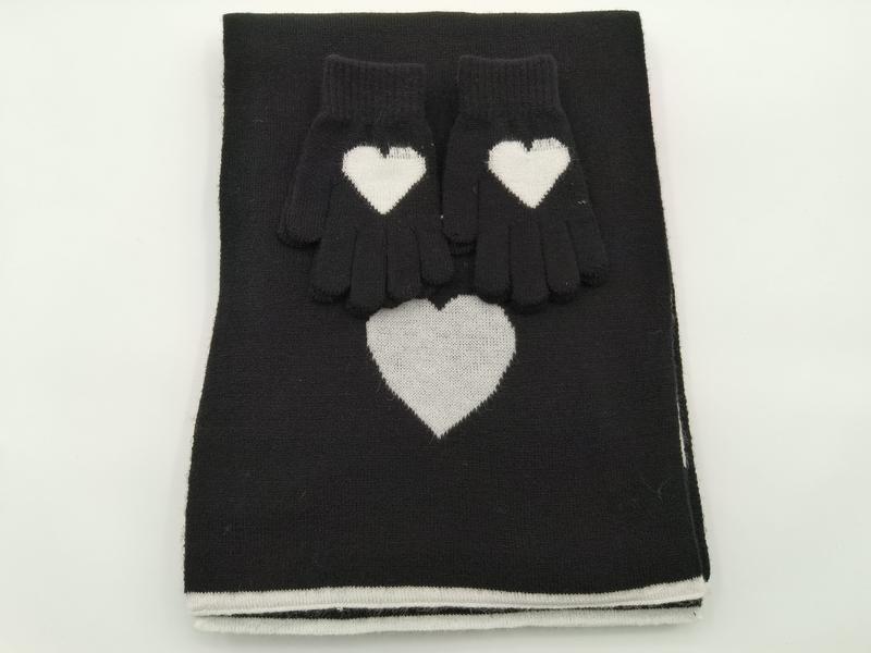 Schwarzes Strick-Set aus gefaltetem Schal und Handschuhen mit weißem Intarsia-Herzmuster auf weißem Hintergrund