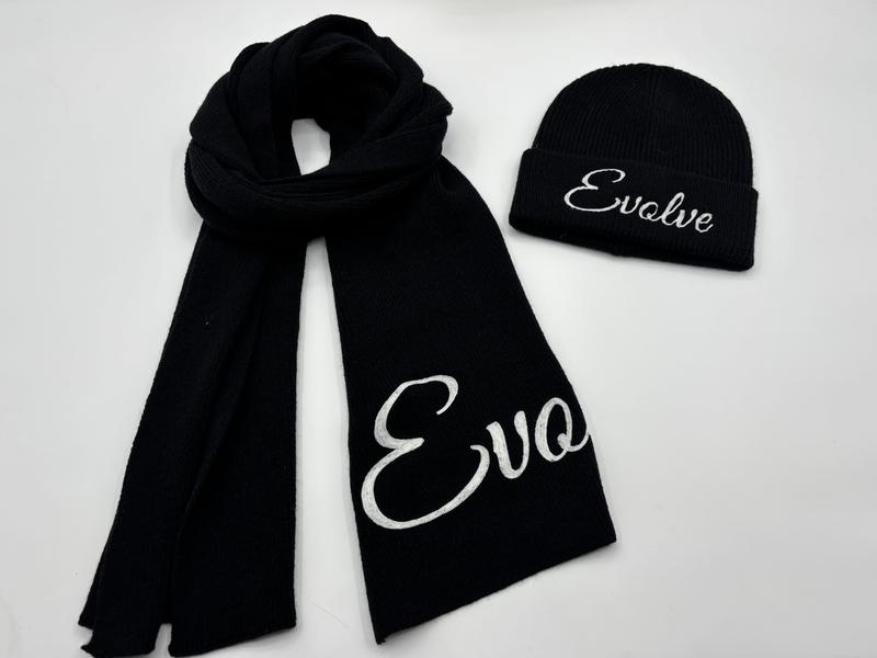 Schwarzes Rippenstrick-Winterset aus Schal und Beanie-Mütze mit weißem bestickten Kursivschrift-Aufdruck auf weißem Hintergrund