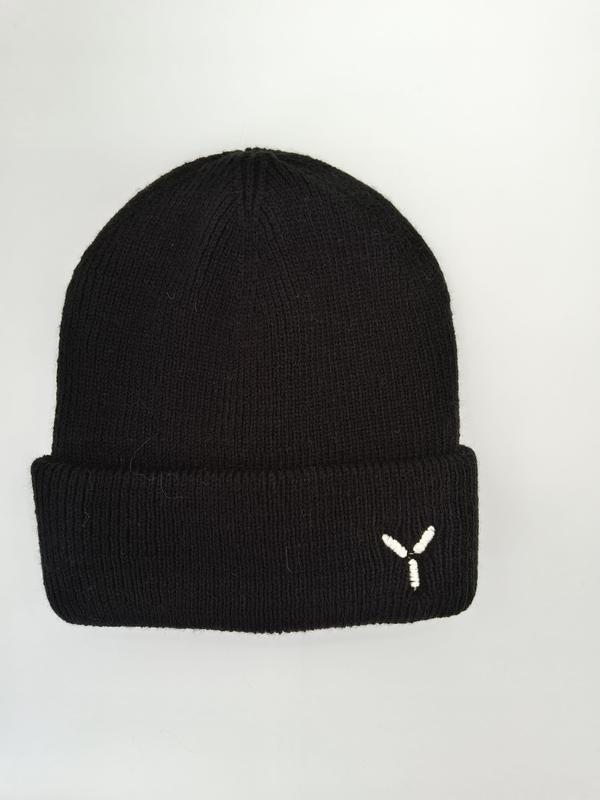 Schwarze Rippenstrickmütze mit Umschlagbündchen und kleinem weißem gestickten Y-Logo auf hellgrauem Hintergrund