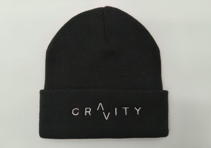 Schwarze Rippenstrick-Beanie mit breitem Umschlag und weiß gesticktem GRAVITY-Schriftzug, Flachaufnahme auf weißem Hintergrund