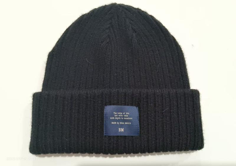 Schwarze gerippte Wintermütze mit breiter Umschlagkrempe und blau gewebtem Label-Patch auf weißem Hintergrund